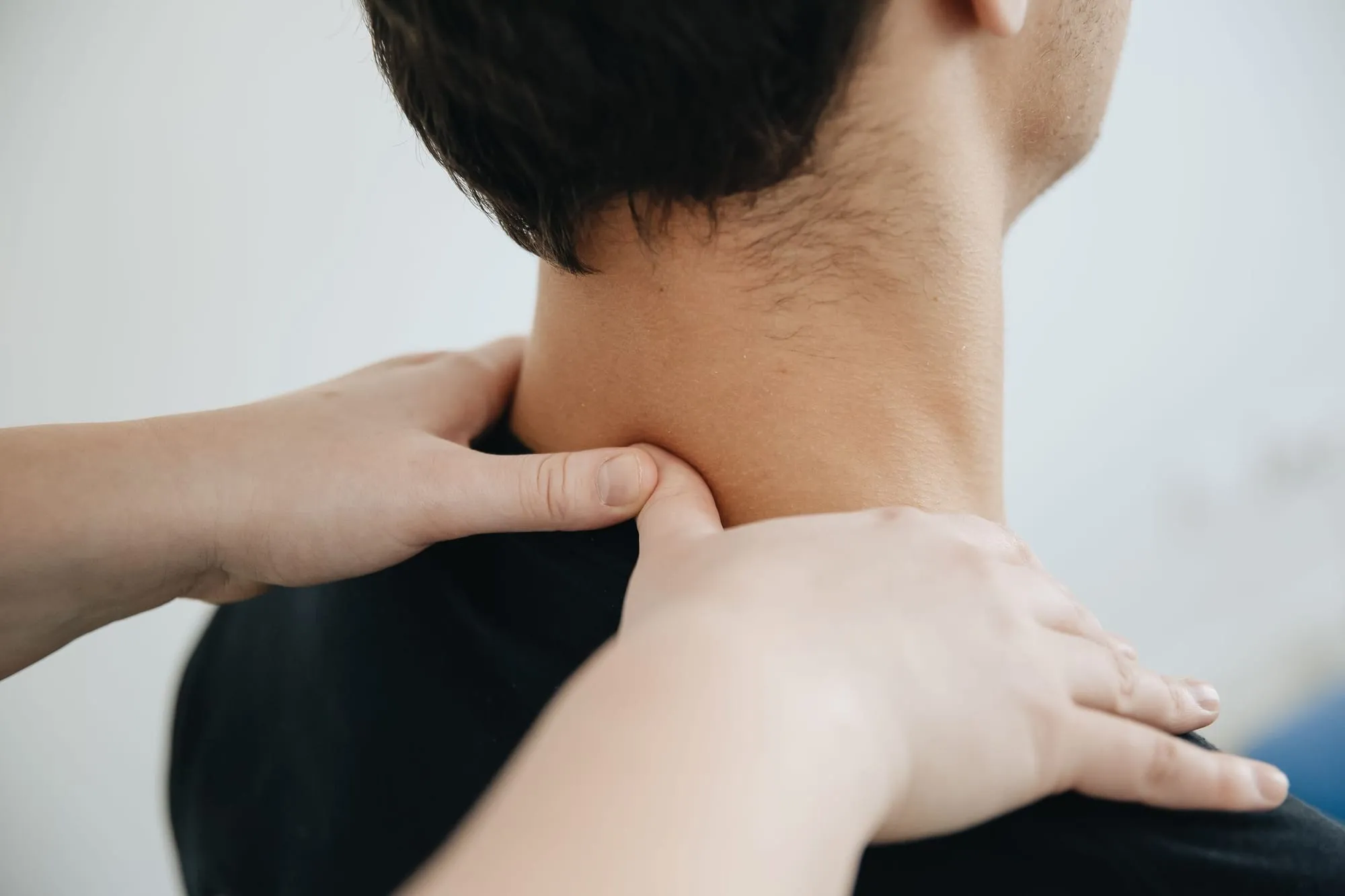 Hände einer Physiotherapeutin an Nacken und Schulter eines Patienten, von hinten gesehen